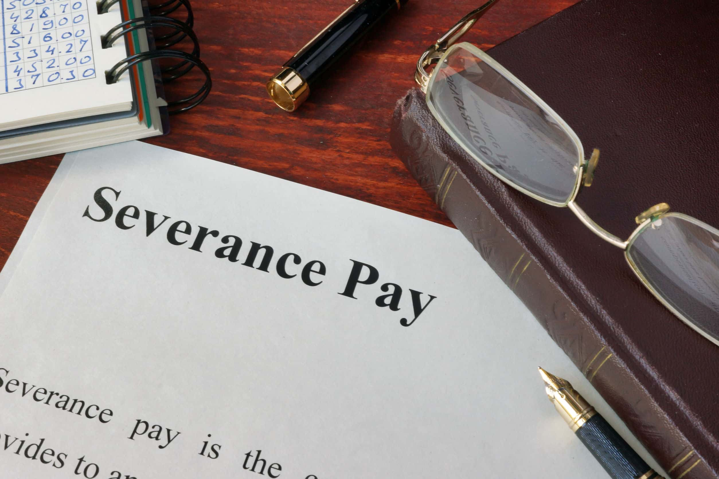 Close-up shot of a 'Severance Pay' document on a wooden desk, beside a notebook with numbers, a pen, and glasses. 