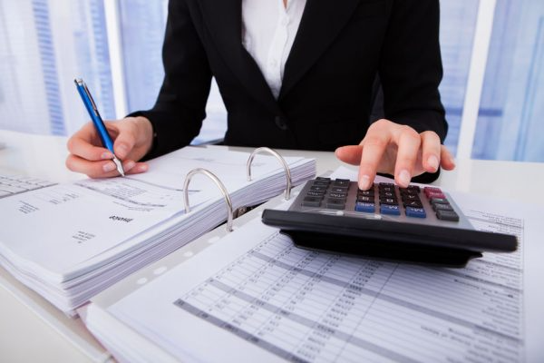 An accountant in a suit reviews invoices with a calculator and pen.